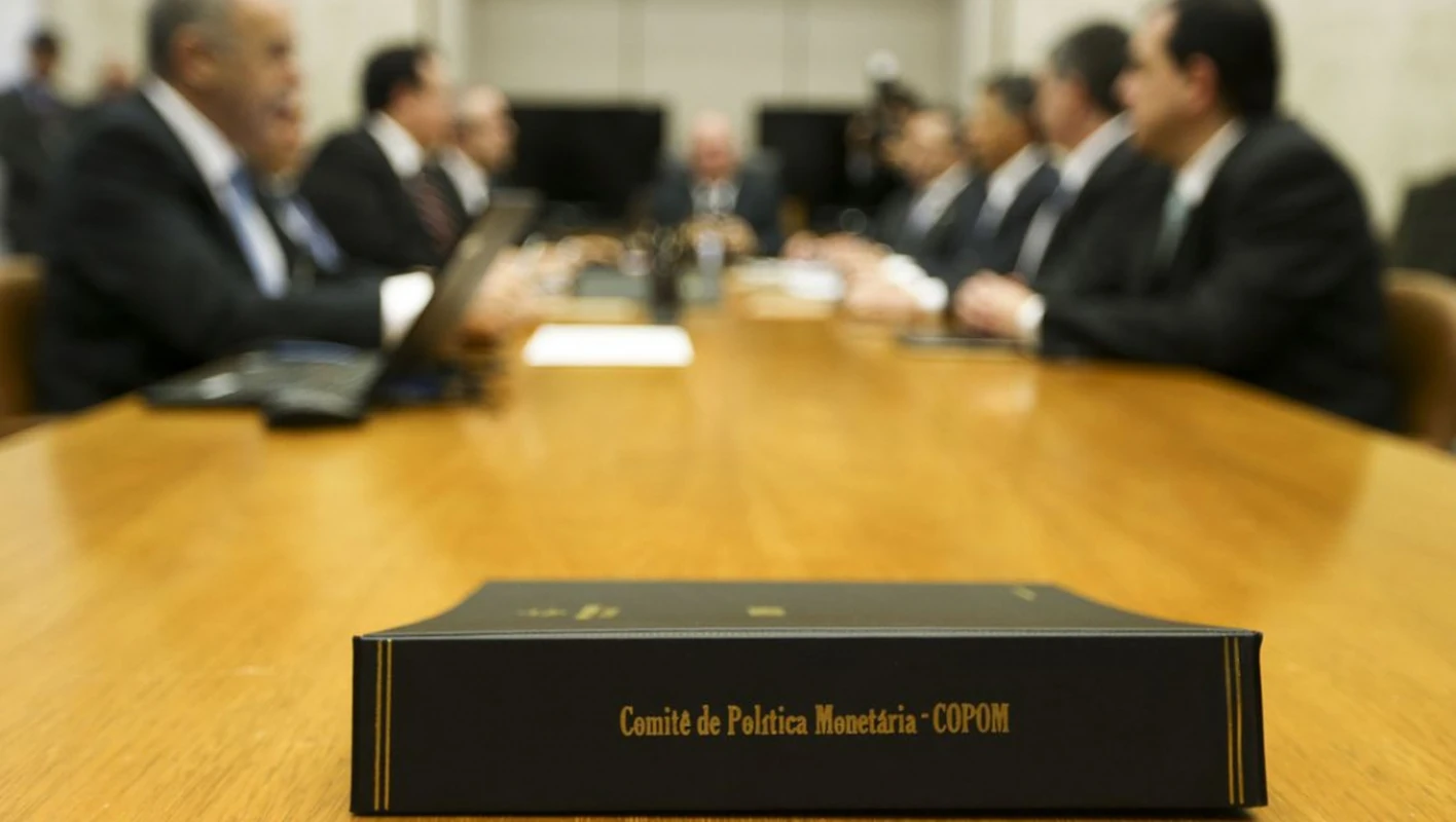 Registro de uma reunião do Copom, com a identificação do Comitê de Política Monetária em primeiro plano.