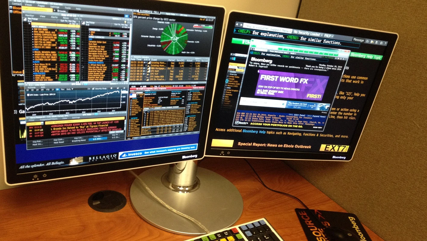 Terminal Bloomberg com dois monitores de dados de mercado, notícias de câmbio e teclado financeiro.